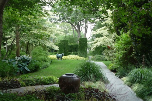 Lush garden with greenery, hedges, and a decorative pot in the foreground, creating a serene outdoor space.