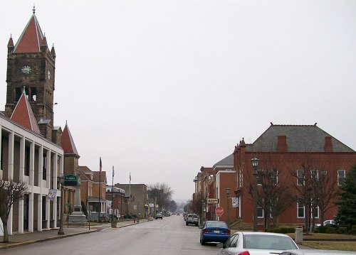 A quiet street scene featuring a clock tower, brick buildings, and a cloudy sky.