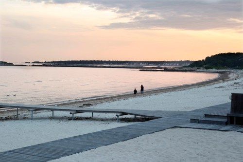 A serene beach at sunset with two people walking along the shore and wooden pathways leading to the water.