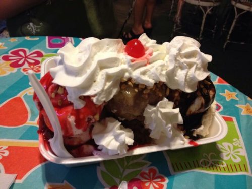 A colorful ice cream sundae topped with whipped cream, nuts, a cherry, and various sauces in a white dish.