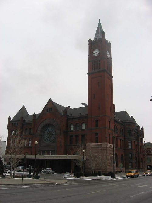 Historic red brick building with a tall clock tower, featuring intricate architectural details and a large circular window.