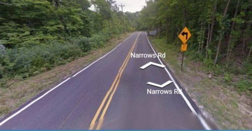 Curved road sign indicating a right turn ahead, surrounded by trees and greenery. Road labeled "Narrows Rd."