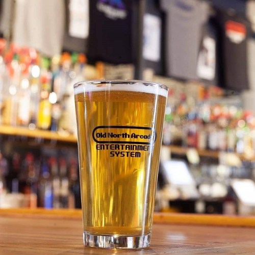 A pint of beer in a glass with "Old North Arcade Entertainment System" logo, set against a bar backdrop.