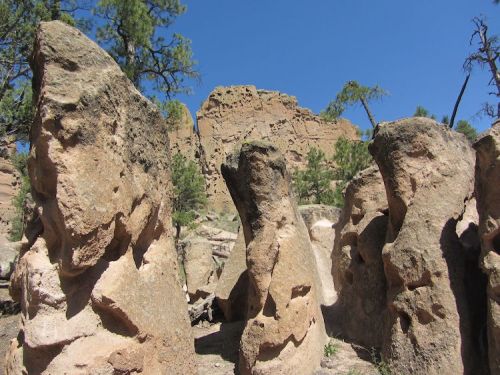 Rock formations rise amidst trees under a clear blue sky, showcasing natural textures and rugged terrain.