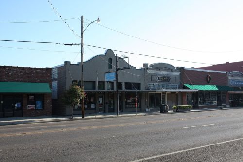 A quiet street scene featuring historic storefronts with green awnings and a clear blue sky.