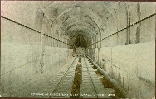 Interior view of the Detroit River Tunnel, showing tracks and tunnel walls in a vintage postcard style.