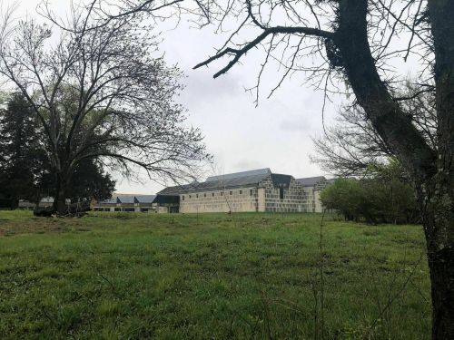 A modern building with large windows, surrounded by trees and grassy fields under a cloudy sky.