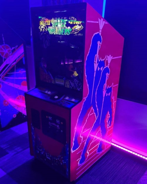 A brightly lit arcade cabinet featuring "Space Invaders" with colorful graphics and a retro design.
