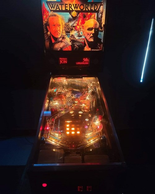 A pinball machine themed after "Waterworld," featuring vibrant lights and a detailed playfield.