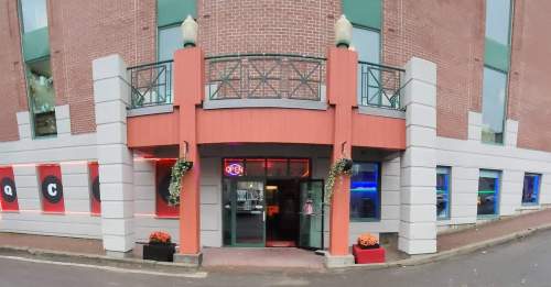 A modern building entrance with an "Open" sign, colorful windows, and decorative plants on the exterior.