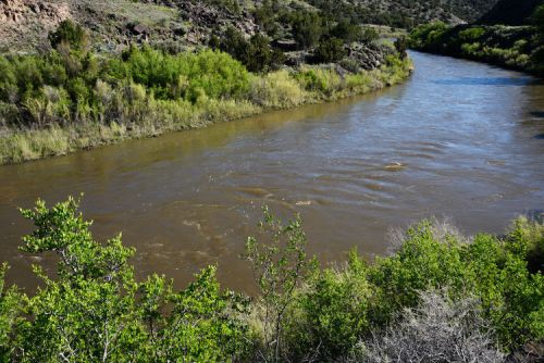 A winding river flows through lush greenery and rocky terrain under a clear blue sky.