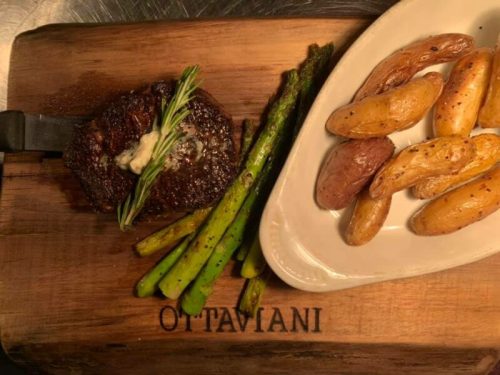 A grilled steak with herbs, asparagus, and roasted potatoes on a wooden serving board.