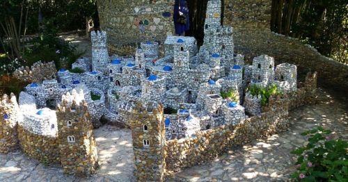 A miniature stone castle with blue-topped towers, surrounded by greenery and pathways.