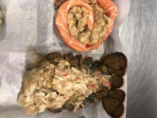A plate featuring a lobster tail stuffed with crab meat and a salmon roll with seafood stuffing.