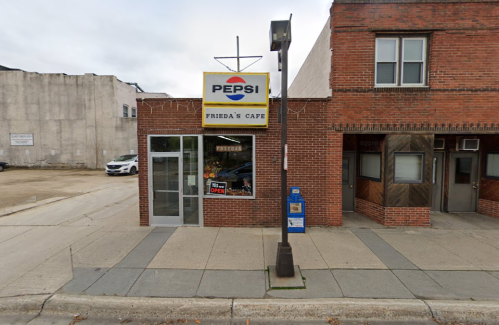Exterior view of Frieda's Cafe, featuring a Pepsi sign, brick facade, and a sidewalk with a streetlamp.