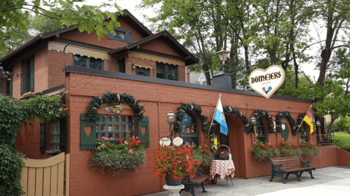 A charming restaurant with a brick exterior, decorated with flowers and festive ornaments, surrounded by greenery.
