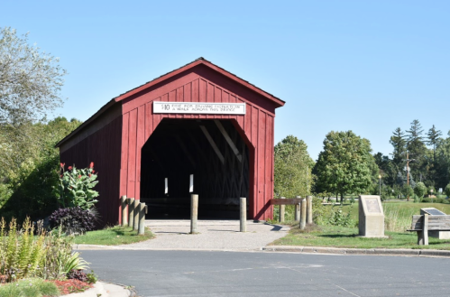 A red covered bridge with a sign, surrounded by greenery and a clear blue sky.