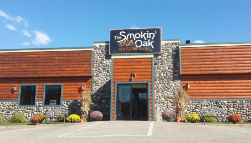 Exterior of The Smokin' Oak Rotisserie & Grill, featuring a stone and wood facade, with colorful flowers in front.