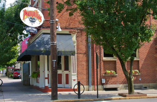 A brick building with a sign reading "Pompili's" and an awning, surrounded by trees and a sidewalk.