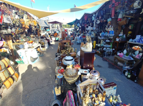 A bustling outdoor market filled with various antiques and collectibles, with stalls and items lining the pathway.