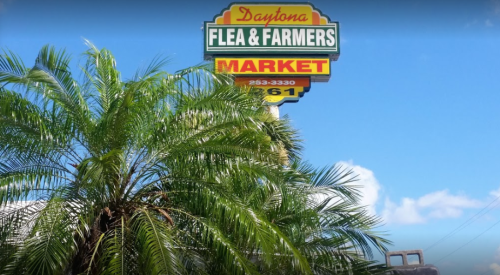 Sign for Daytona Flea & Farmers Market with palm trees and a blue sky in the background.