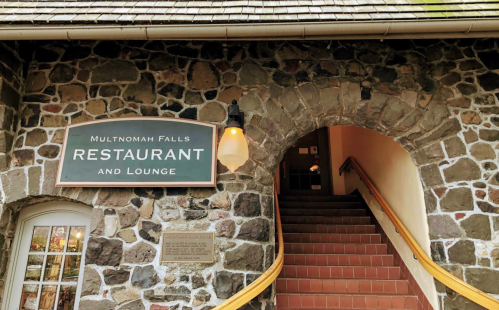 Stone building entrance with a sign reading "Multnomah Falls Restaurant and Lounge" and stairs leading up.
