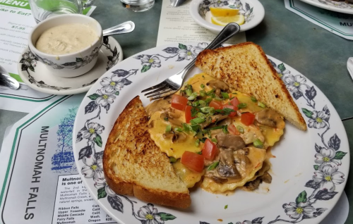 A plate of omelette with mushrooms and tomatoes, served with toast, alongside a bowl of clam chowder.