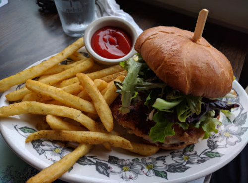 A crispy chicken sandwich topped with lettuce, served with a side of golden fries and a small dish of ketchup.