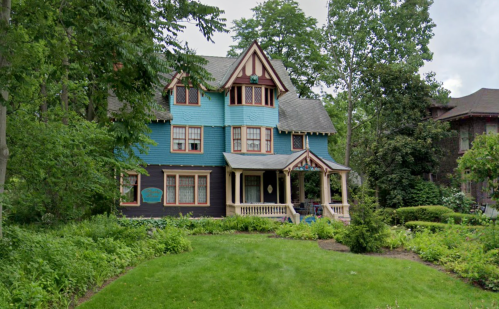 A colorful Victorian-style house surrounded by lush greenery and trees.