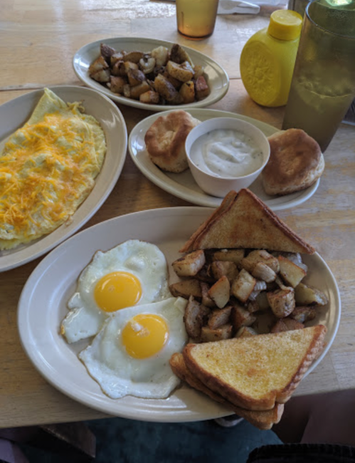 A hearty breakfast spread featuring an omelette, fried eggs, potatoes, toast, biscuits, and a side of yogurt.