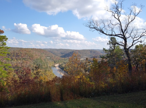 Scenic view of a river winding through autumn-colored hills under a partly cloudy sky.