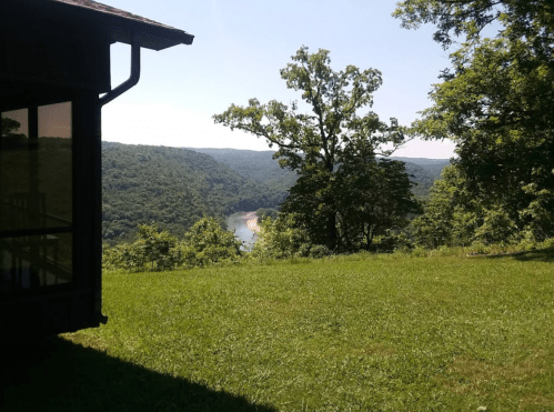 A scenic view of a river winding through green hills, framed by trees and a building in the foreground.
