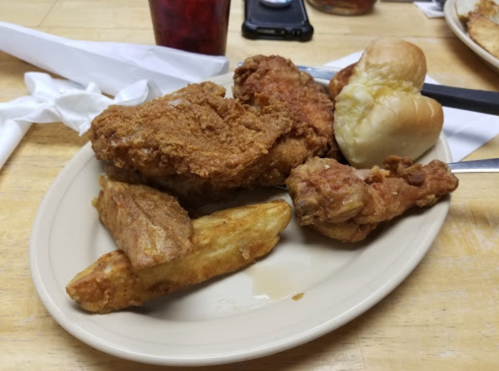 A plate of fried chicken, potato wedges, and dinner rolls on a wooden table.
