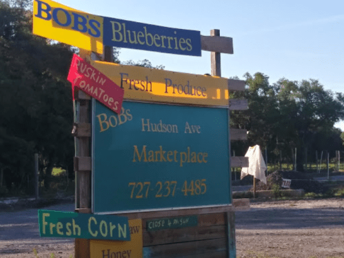 Signpost for Bob's Marketplace featuring fresh blueberries, corn, and tomatoes, with contact information and hours.