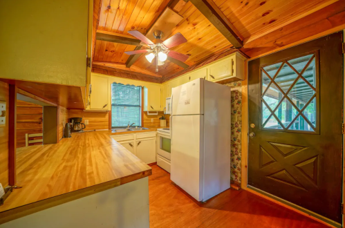 Cozy kitchen with wooden ceiling, white appliances, and a door leading outside. Bright and inviting atmosphere.
