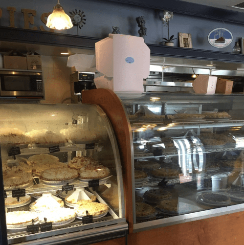 Display case filled with various pies, showcasing a variety of flavors in a cozy bakery setting.