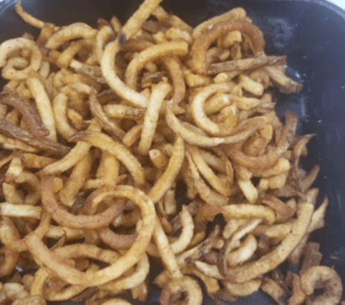 A close-up of crispy, golden-brown curly fries piled in a black container.