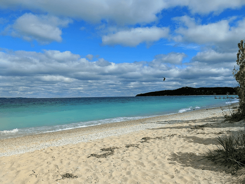 A serene beach scene with soft sand, gentle waves, and a cloudy blue sky in the background.