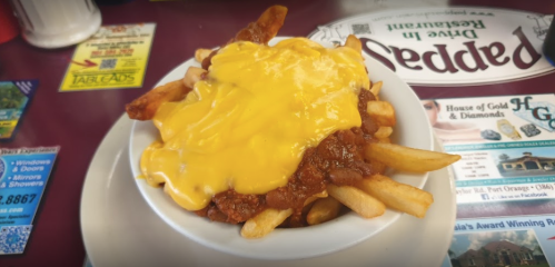 A bowl of fries topped with chili and melted cheese, served in a casual diner setting.