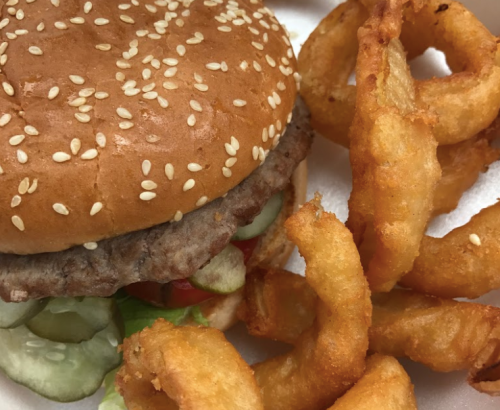 A sesame seed bun burger with lettuce, pickles, and tomatoes, accompanied by crispy onion rings.