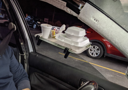 A makeshift food tray attached to a car window, holding takeout containers and a drink.