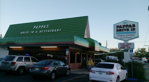Exterior of Pappas Drive-In & Restaurant, featuring a green roof, neon signs, and parked cars in front.