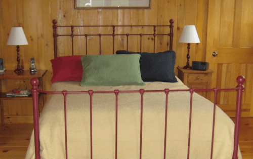 A cozy bedroom featuring a metal bed frame with colorful pillows, a yellow bedspread, and wooden walls.
