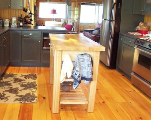 A cozy kitchen with wooden floors, a central island, and gray cabinets, featuring a rug and various kitchen items.