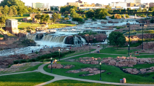 A scenic view of waterfalls cascading over rocks, surrounded by greenery and people enjoying the park.