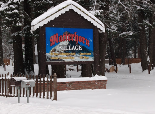 Sign for "Matterhorn Village" surrounded by snow-covered trees and a white landscape.