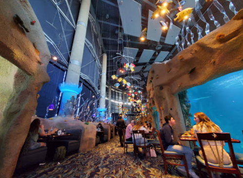 A vibrant restaurant interior with underwater decor, featuring colorful fish and diners enjoying their meals.