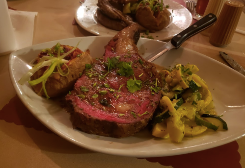 A plate featuring a juicy ribeye steak, baked potato with toppings, and sautéed zucchini and squash.