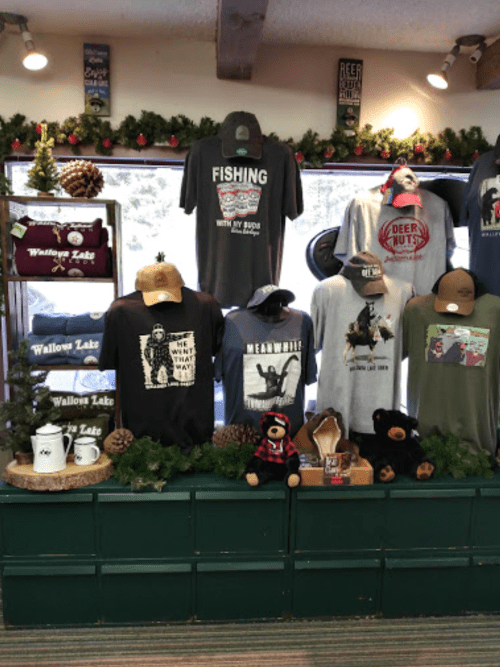 Display of various t-shirts and hats featuring outdoor themes, set against a festive, decorated backdrop.