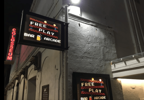 Sign for a bar arcade featuring "Free Play" in neon lights, with a retro gaming theme, at night.